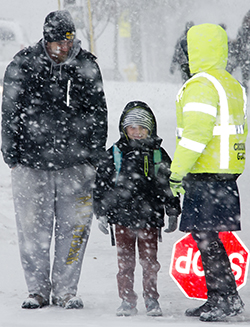 Patrick Scranton picks up his son, Jaxon, and chats with Kattie Eason, before she helps them cross a busy Wealthy Street SE in a snow storm
