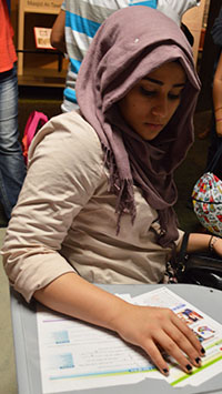 Newcomer student Zainab Ahmed sits at a school desk in the immigration exhibit